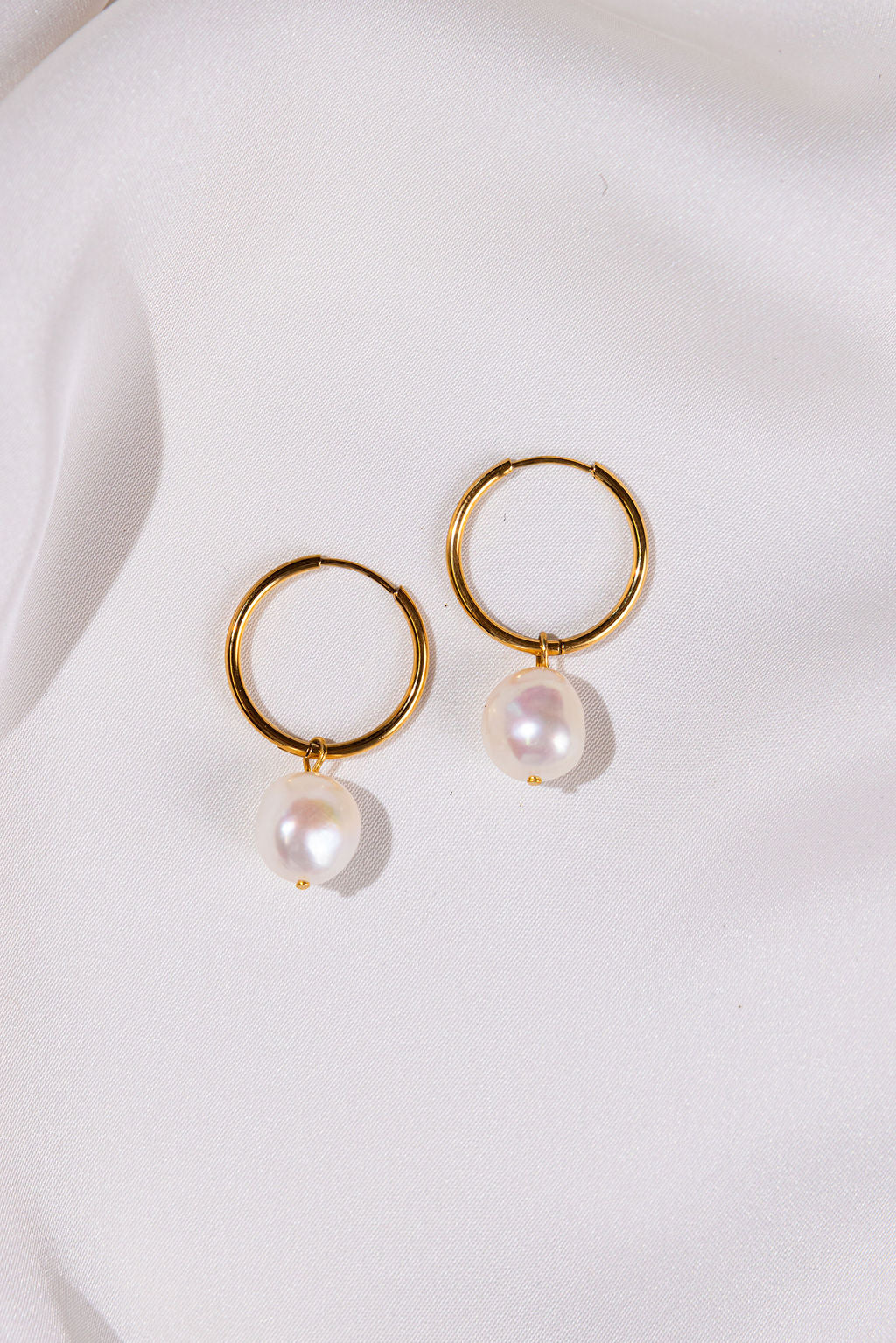 Gold hoop earrings with pearl drops on a white background