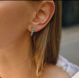Close-up of an ear wearing turquoise hoop earrings with blurred background
