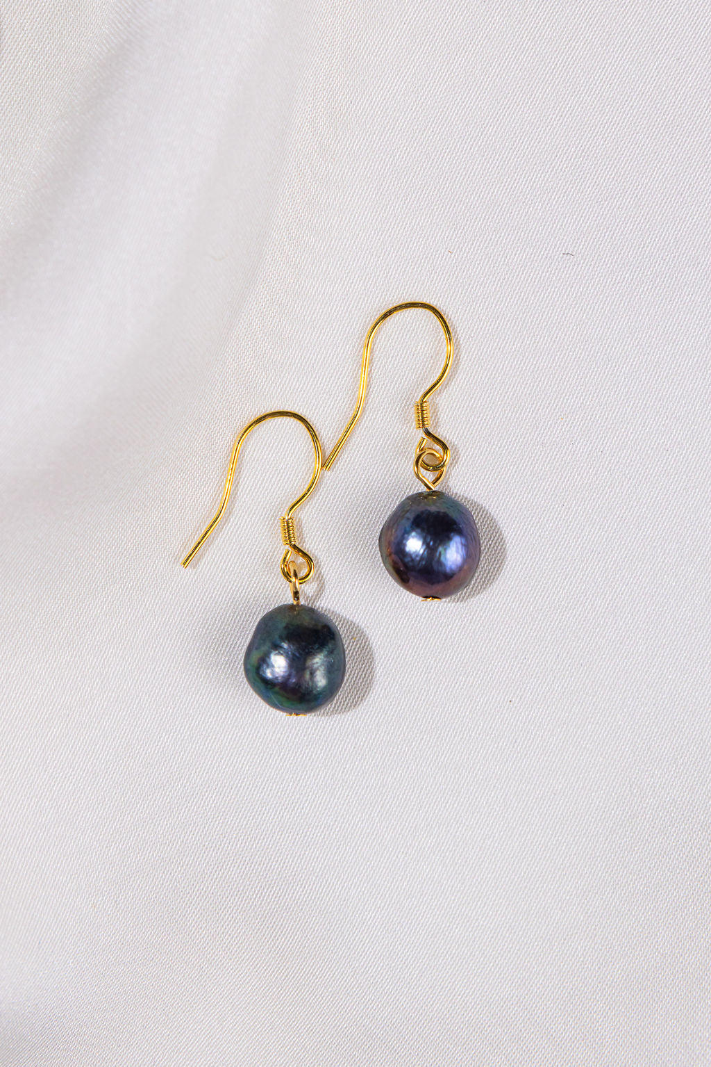 Pair of black pearl earrings with gold hooks on a light gray background