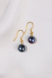 Pair of black pearl earrings with gold hooks on a light gray background
