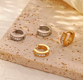 Set of gold and silver hoop earrings on a textured stone surface