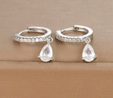 Silver hoop earrings with teardrop-shaped crystals on a beige surface
