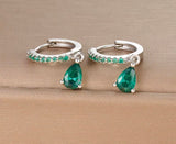 Pair of silver hoop earrings with green teardrop gemstones on a beige surface