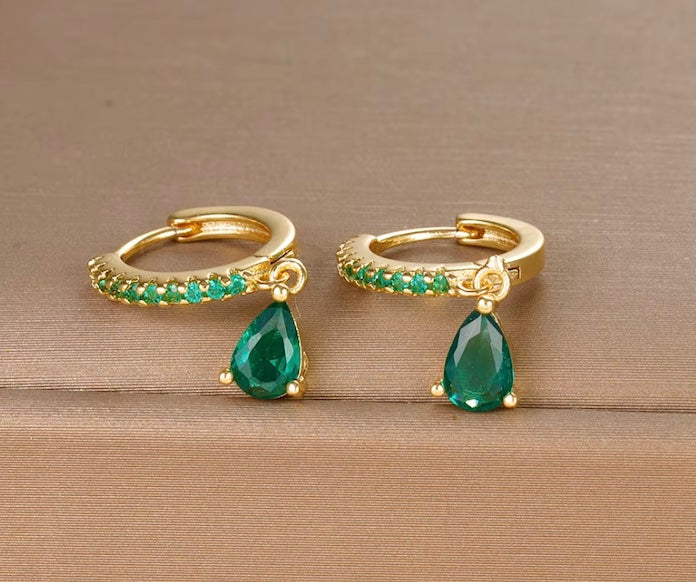Gold hoop earrings with green teardrop gemstones on a wooden surface