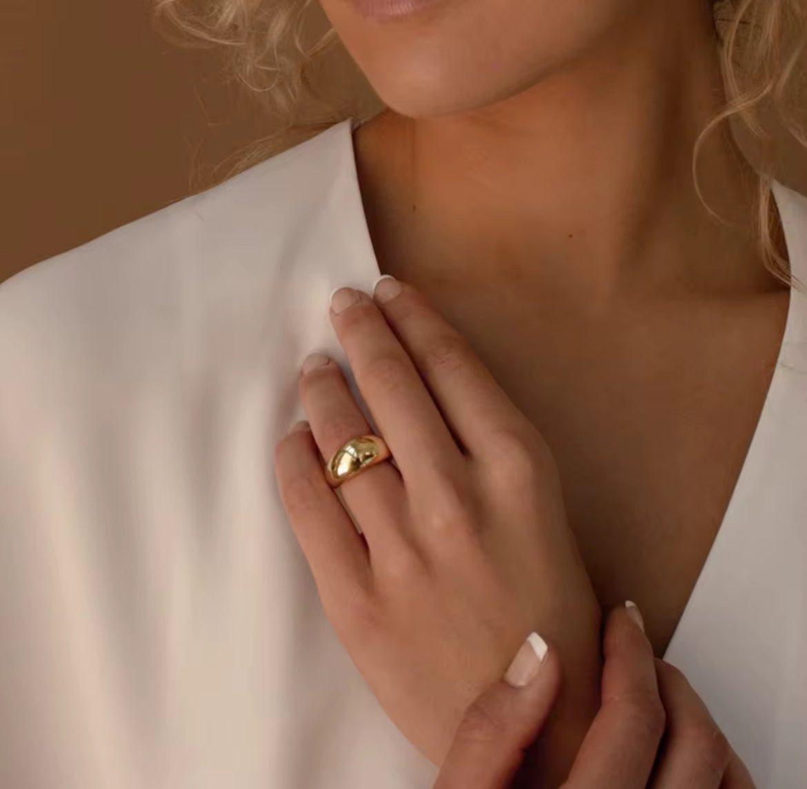 Close-up of a person wearing a gold ring on a neutral background