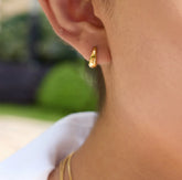 Close-up of a person wearing a gold hoop earring with a blurred outdoor background