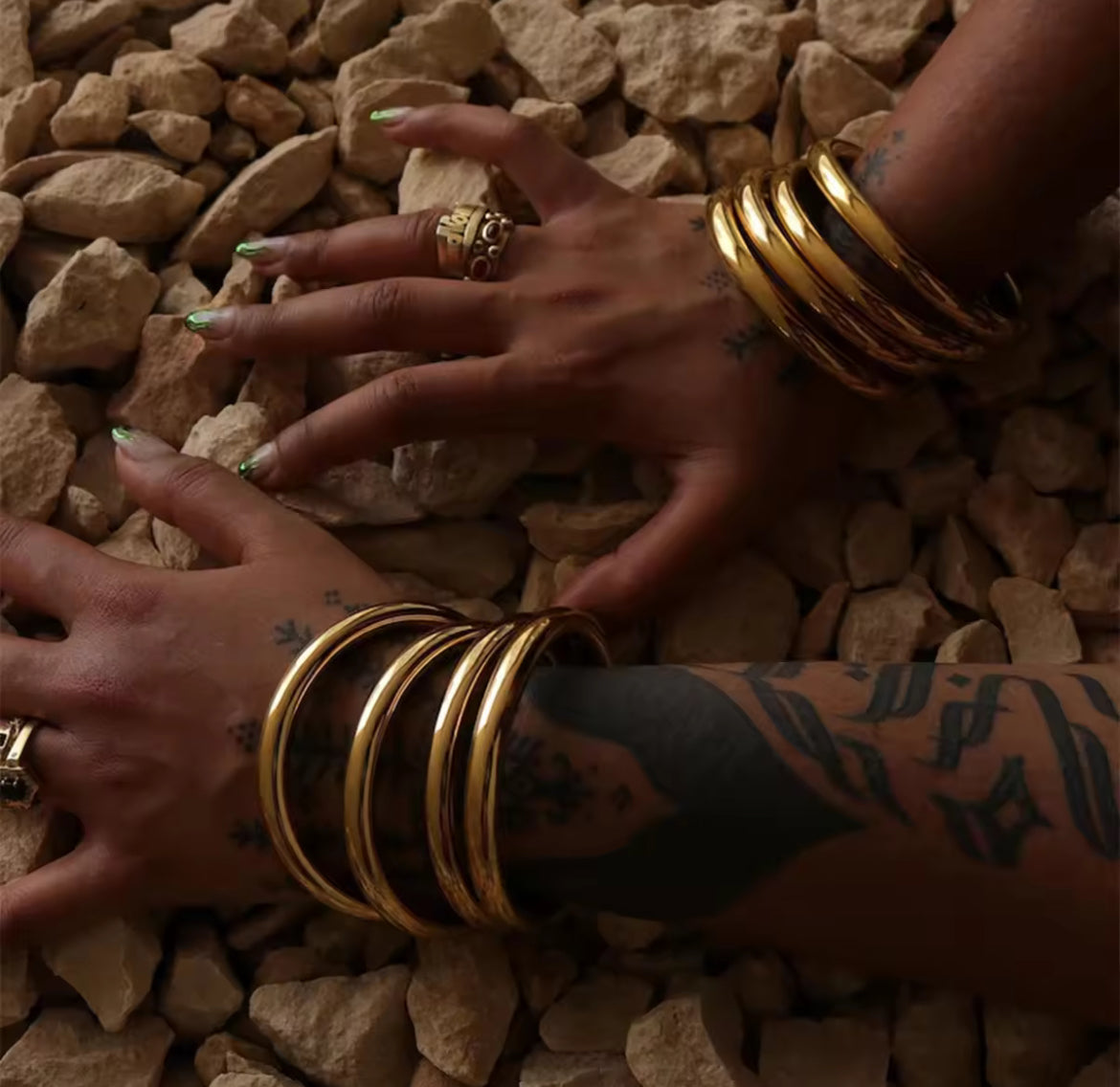 Hands with gold bracelets and tattoos on a rocky surface