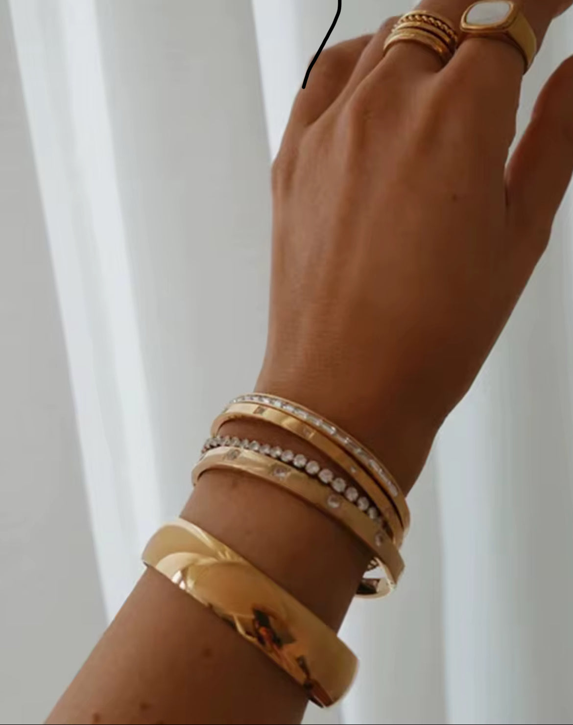 Hand wearing multiple gold bracelets on a white background