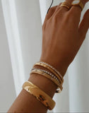 Hand wearing multiple gold bracelets on a white background