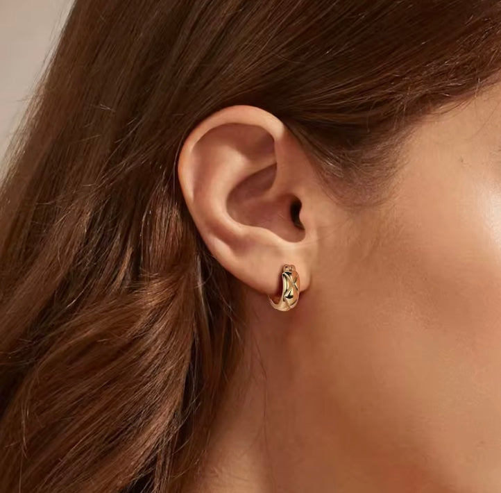 Close-up of an ear wearing a gold earring with brown hair and skin in the background