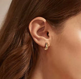 Close-up of an ear wearing a gold earring with brown hair and skin in the background
