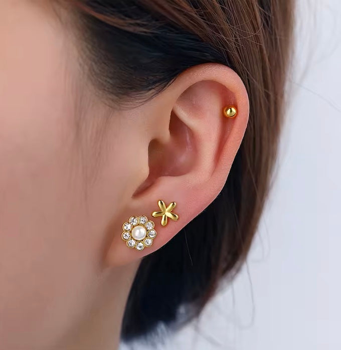 Close-up of an ear wearing gold earrings with floral designs.