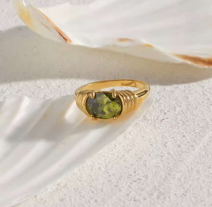 Gold ring with a green gemstone on a white shell background