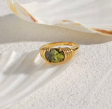 Gold ring with a green gemstone on a white shell background