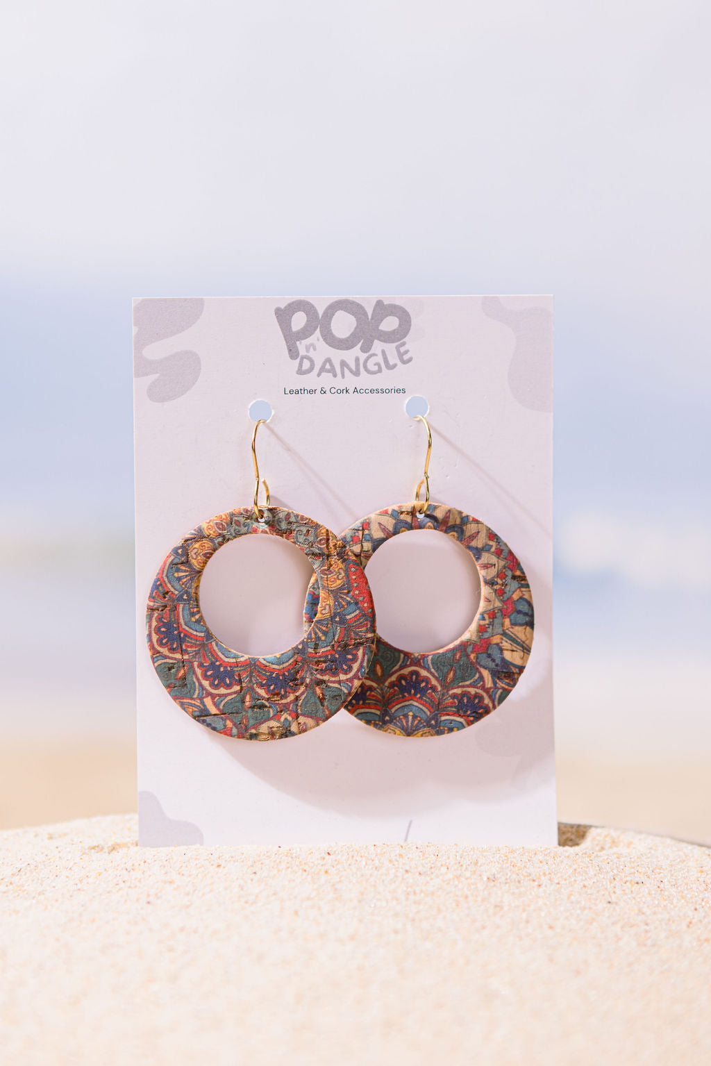 Decorative earrings on a 'Pop Dangle' branded card with a beach background