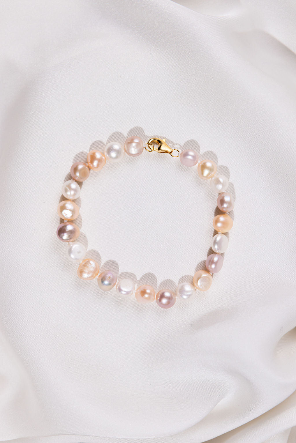 Mixed Pearl bracelet with gold clasp on a white fabric background