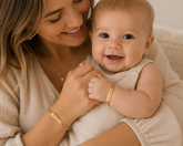 Woman holding a baby and smiling, both wearing gold bracelets