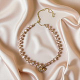 Pearl necklace with gold shel charm on a soft pink fabric background