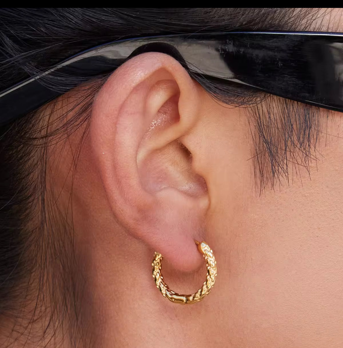Close-up of an ear wearing a gold hoop earring with sunglasses on.