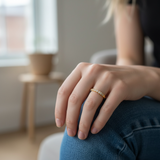 Person wearing a gold ring with a blurred indoor background