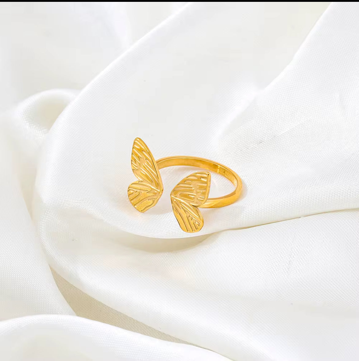 Gold butterfly-shaped ring on a white fabric background