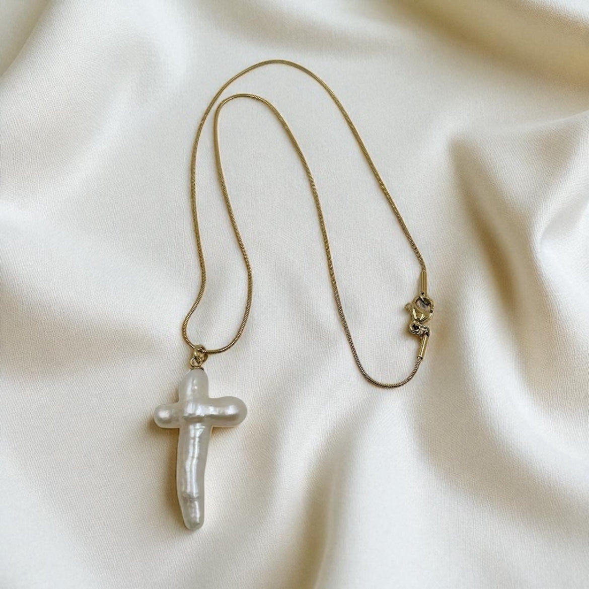 Necklace with a pearl cross pendant on a beige fabric background