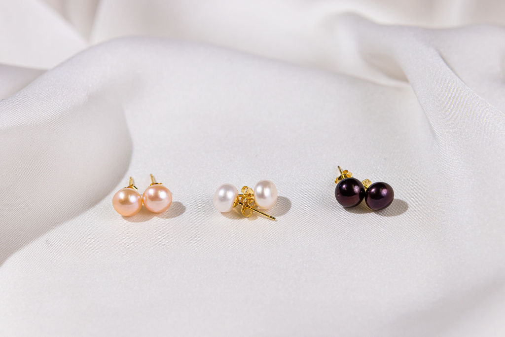 Three pairs of pearl earrings on a white fabric background