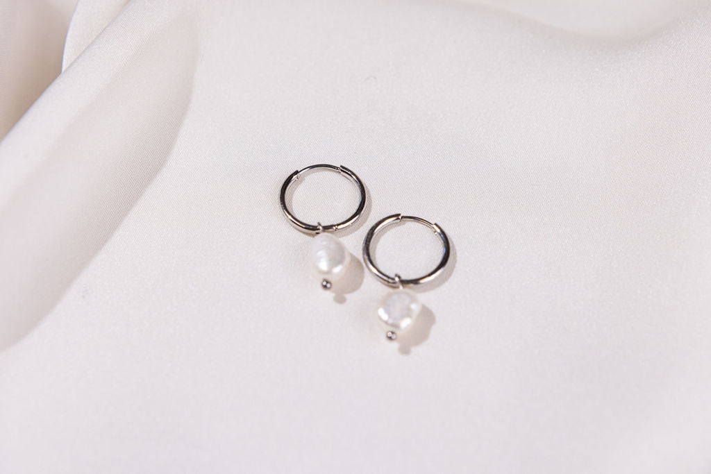 Pair of silver hoop earrings with pearls on a light background