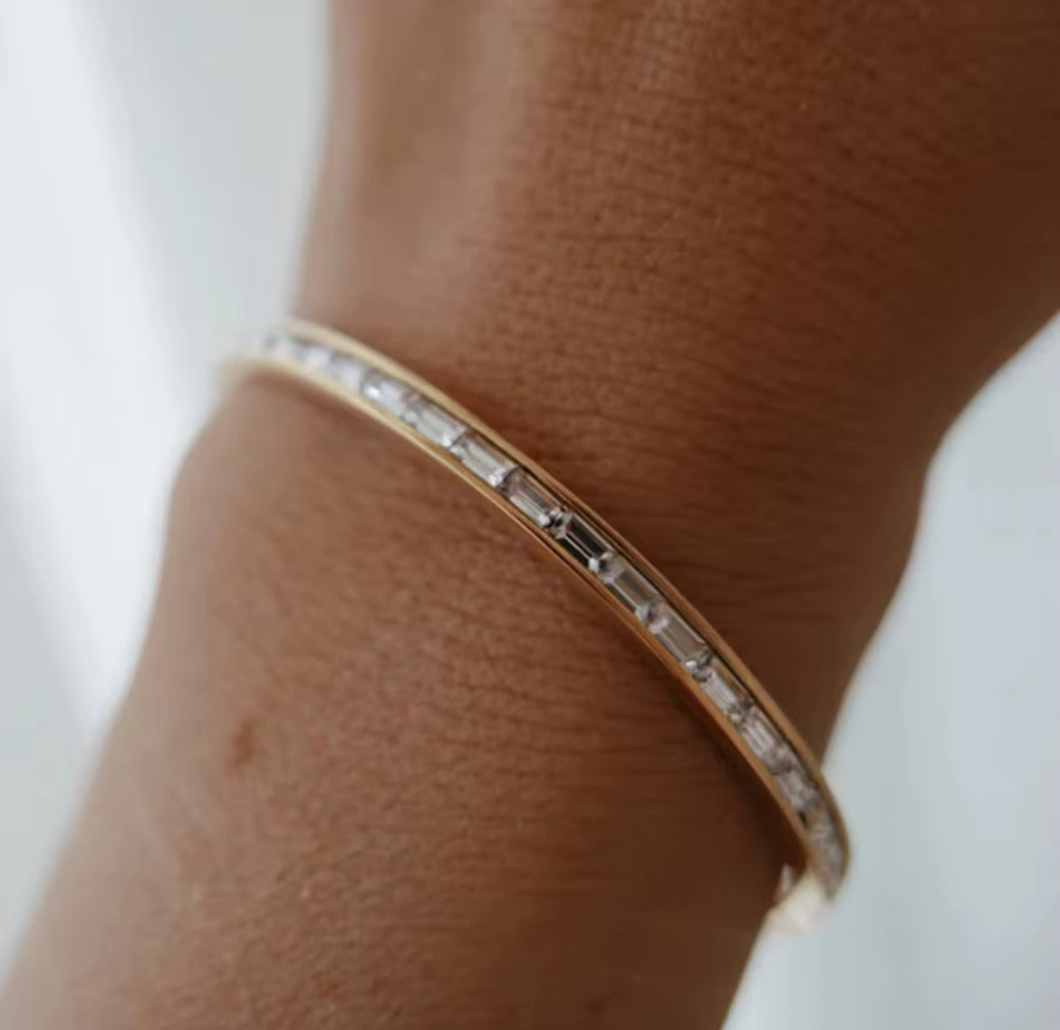 Rose gold bracelet with clear stones on a wrist against a light background