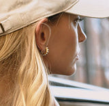Close-up of a person wearing a beige cap and gold hoop earrings, with a blurred background.