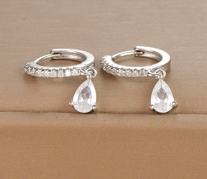 Silver hoop earrings with teardrop-shaped crystals on a beige surface