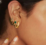 Gold hoop earrings with green gemstones worn by a person.