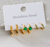 Set of gold hoop earrings with green gemstones on a white card labeled 'Stainless Steel'.