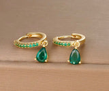 Gold hoop earrings with green teardrop gemstones on a wooden surface