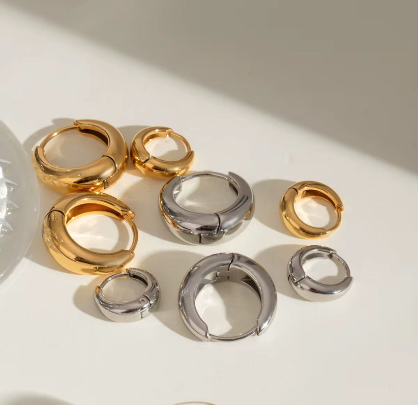 Gold and silver hoop earrings on a light surface with soft shadows.