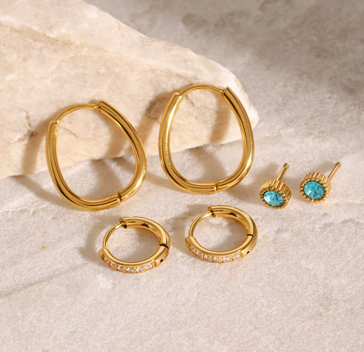 Gold hoop earrings and turquoise stud earrings on a textured beige surface