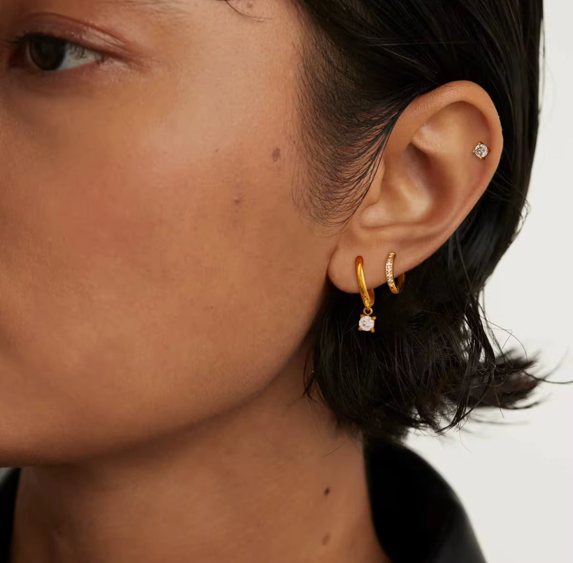 Close-up of a person wearing gold hoop earrings with clear gemstones.