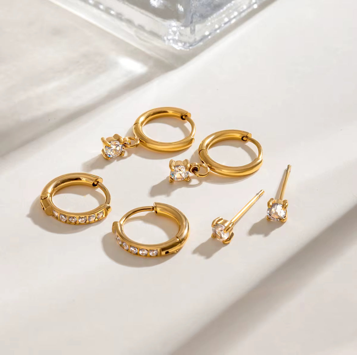 Set of gold hoop earrings with clear gemstones on a light background