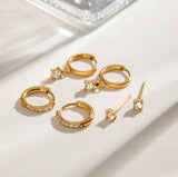 Set of gold hoop earrings with clear gemstones on a light background