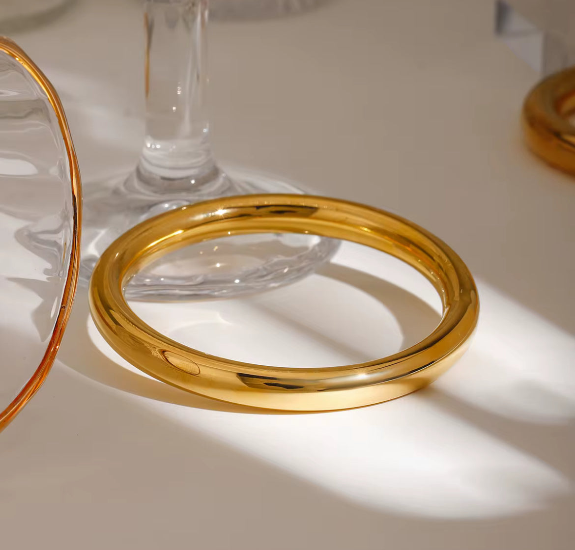 Gold ring on a white surface with a glass object in the background