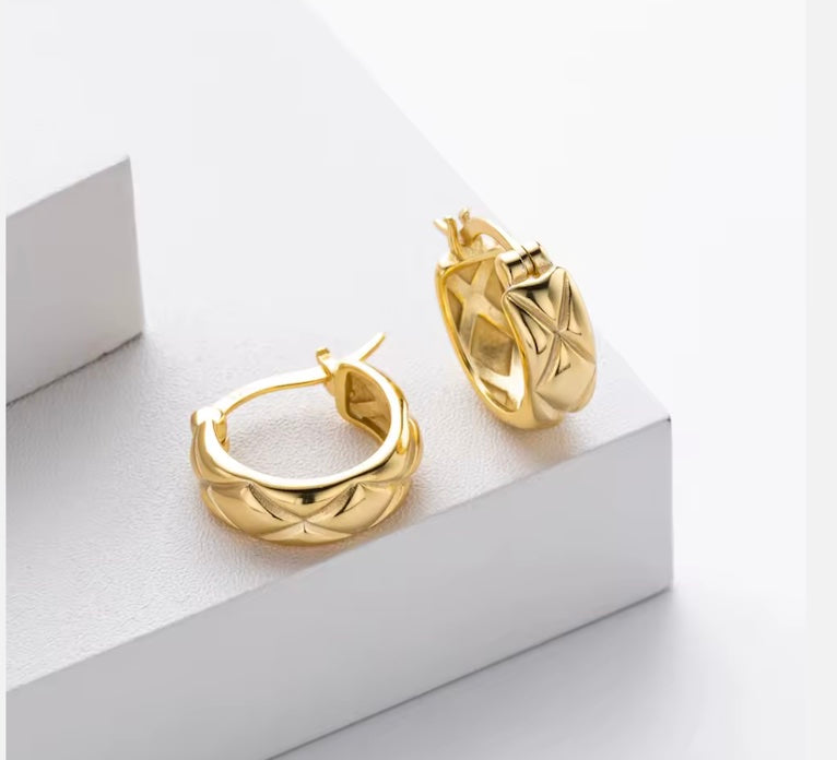 Gold hoop earrings on a white geometric background