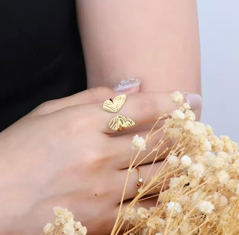 Gold butterfly earrings on a hand with dried flowers