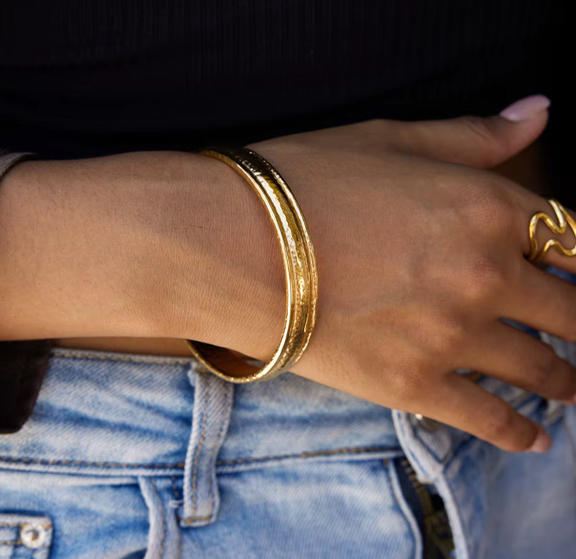 Hand wearing a gold bracelet and ring with a blurred background