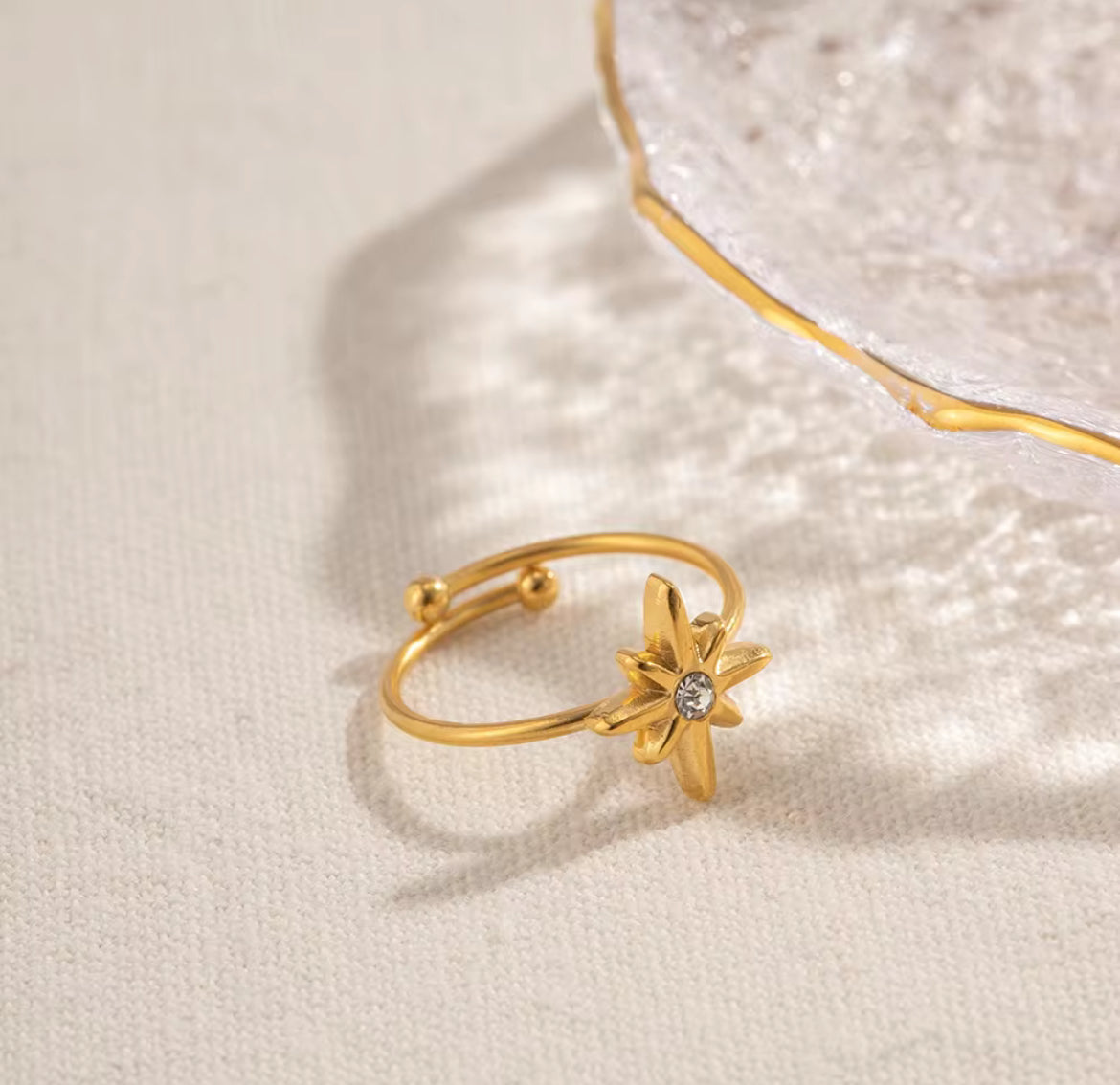 Gold ring with star design and diamond on a beige surface