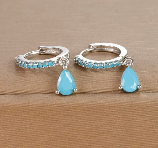 Silver hoop earrings with blue teardrop stones on a beige background