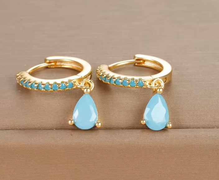 Gold hoop earrings with blue teardrop stones on a wooden surface