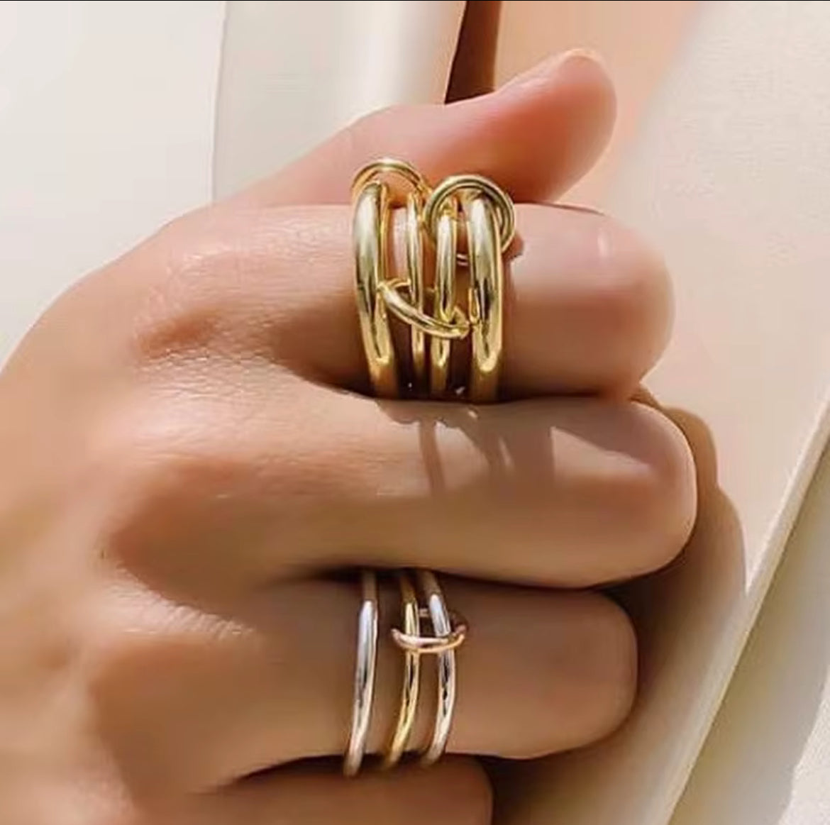 Gold ring with interlocking design on a hand against a neutral background