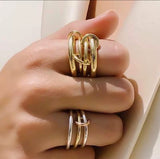 Gold ring with interlocking design on a hand against a neutral background