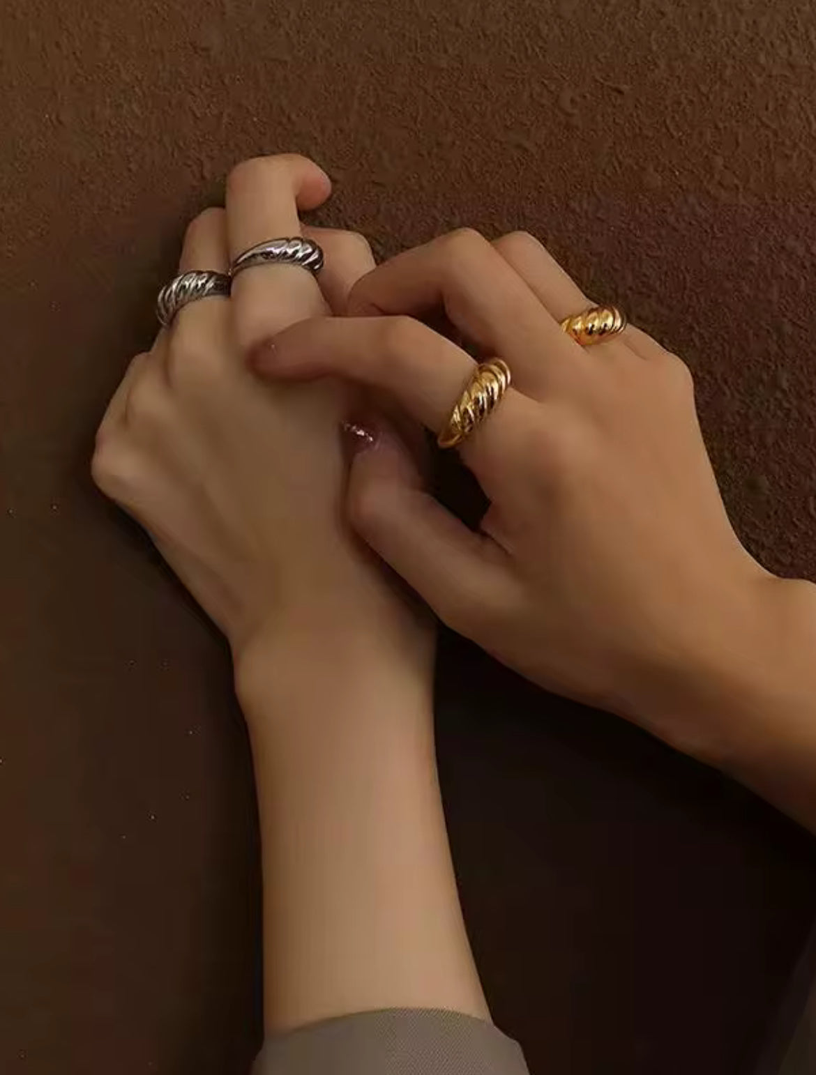 Two hands with rings on a brown background