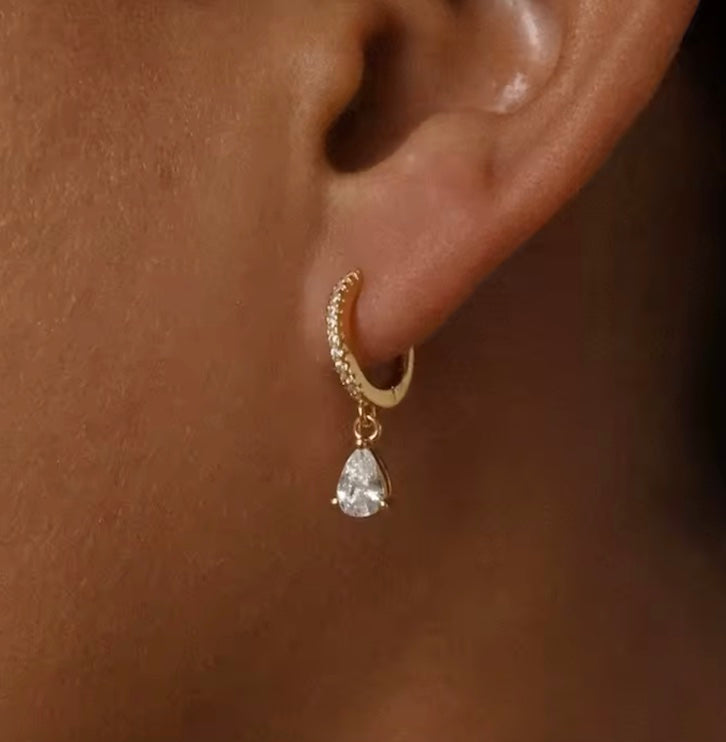 Gold earring with a teardrop-shaped gemstone worn on an ear.